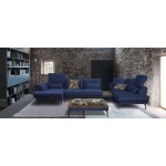 Μπλε γωνιακός καναπές “Roche” τοποθετημένος σε industrial boho loft: πέτρινοι τοίχοι, γκρι μοκέτα και ράφι βιβλιοθήκης. (Thumb 9)